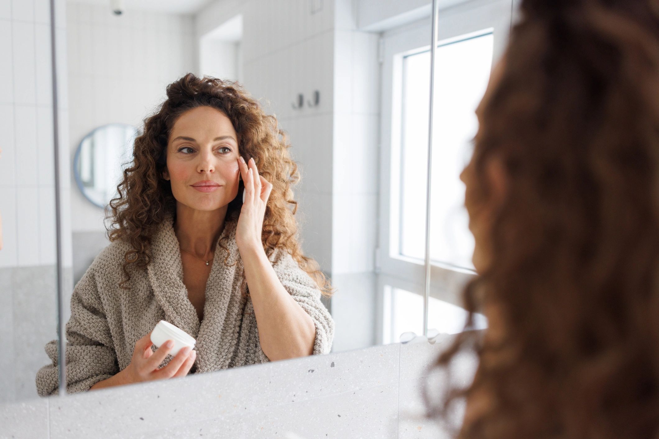 Woman applying skincare cream during a healthy aging routine